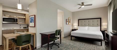 A hotel room with a bed, desk, chair, microwave, and ceiling fan.