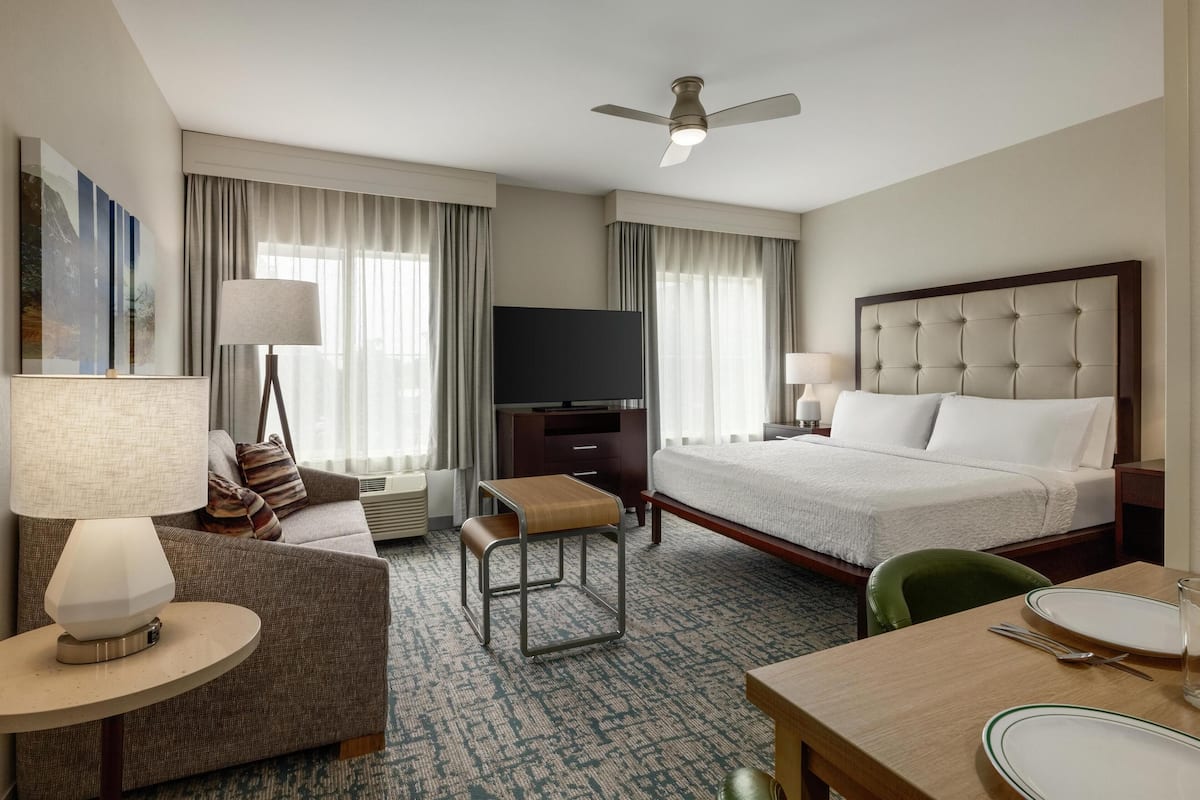 A hotel room with a bed, a TV, a sofa, a table, and a chair.