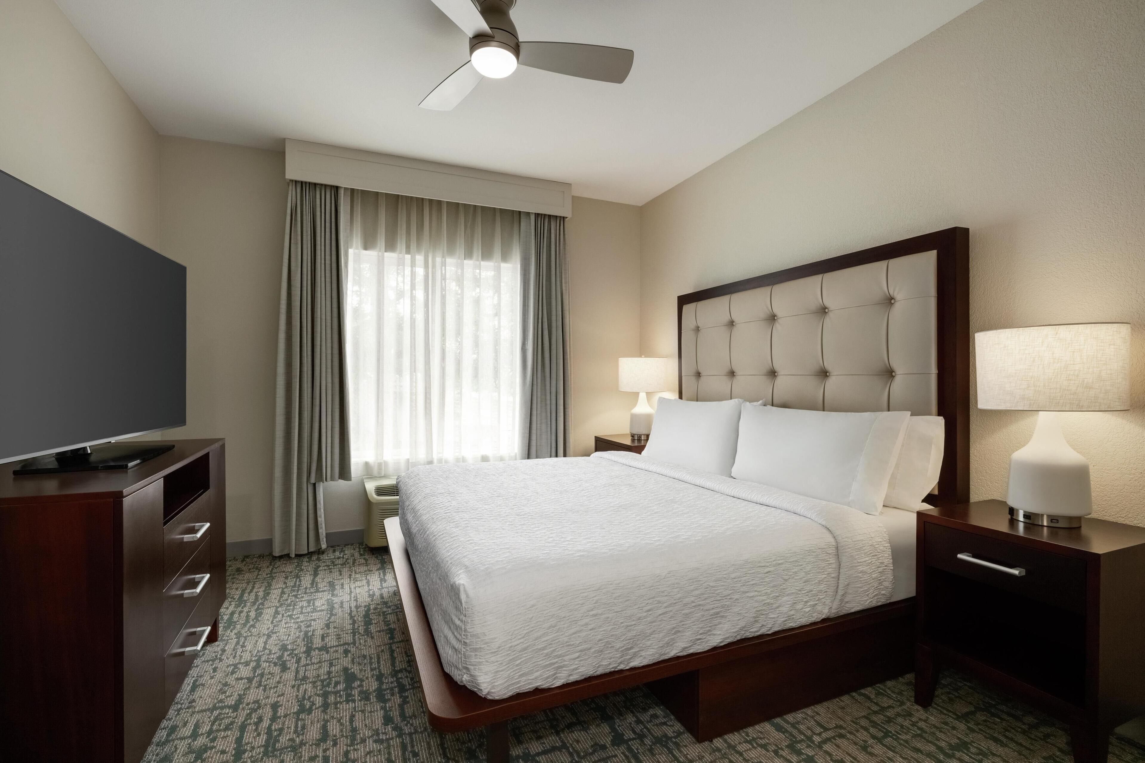A hotel room with a bed, a TV, a desk, and a ceiling fan.