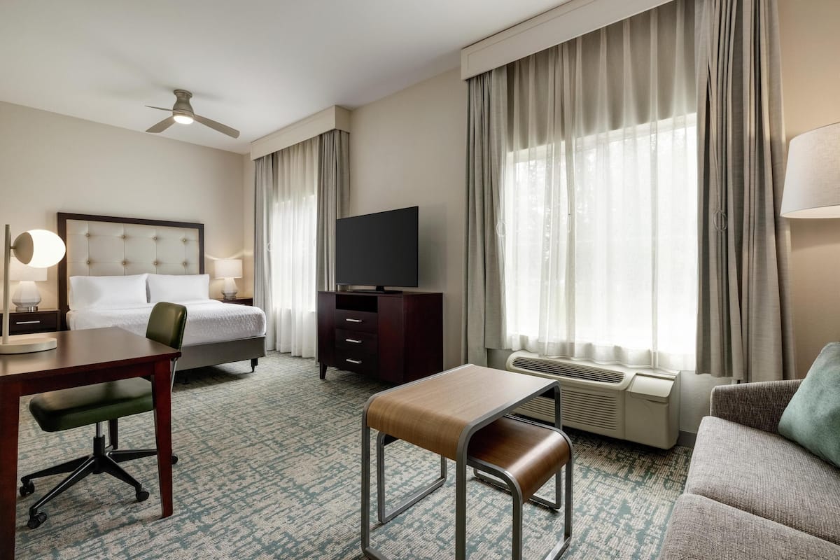 A hotel room with a bed, a desk, a chair, a TV, a dresser, and a sofa.