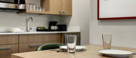 A kitchen with wooden cabinets, a microwave, and a coffee maker. There is a dining table with a glass and a plate.