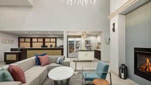 A modern living room with a sectional sofa, a round coffee table, and a fireplace. There is a kitchen area with a refrigerator and a dining table in the background. - Homewood Suites by Hilton Denver West Lakewood (Lakewood)