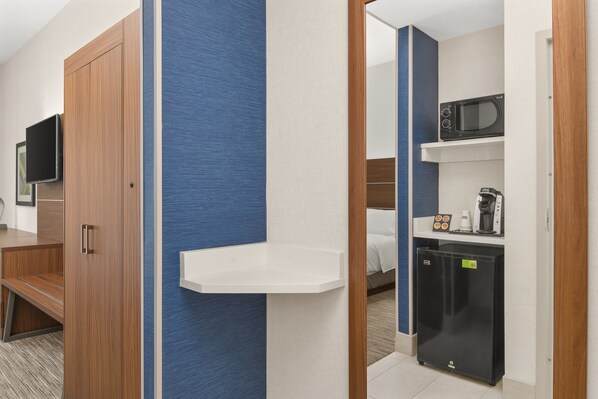 Habitación de hotel con armario de madera, televisor de pantalla plana, kitchenette pequeña con microondas, cafetera y refrigerador.