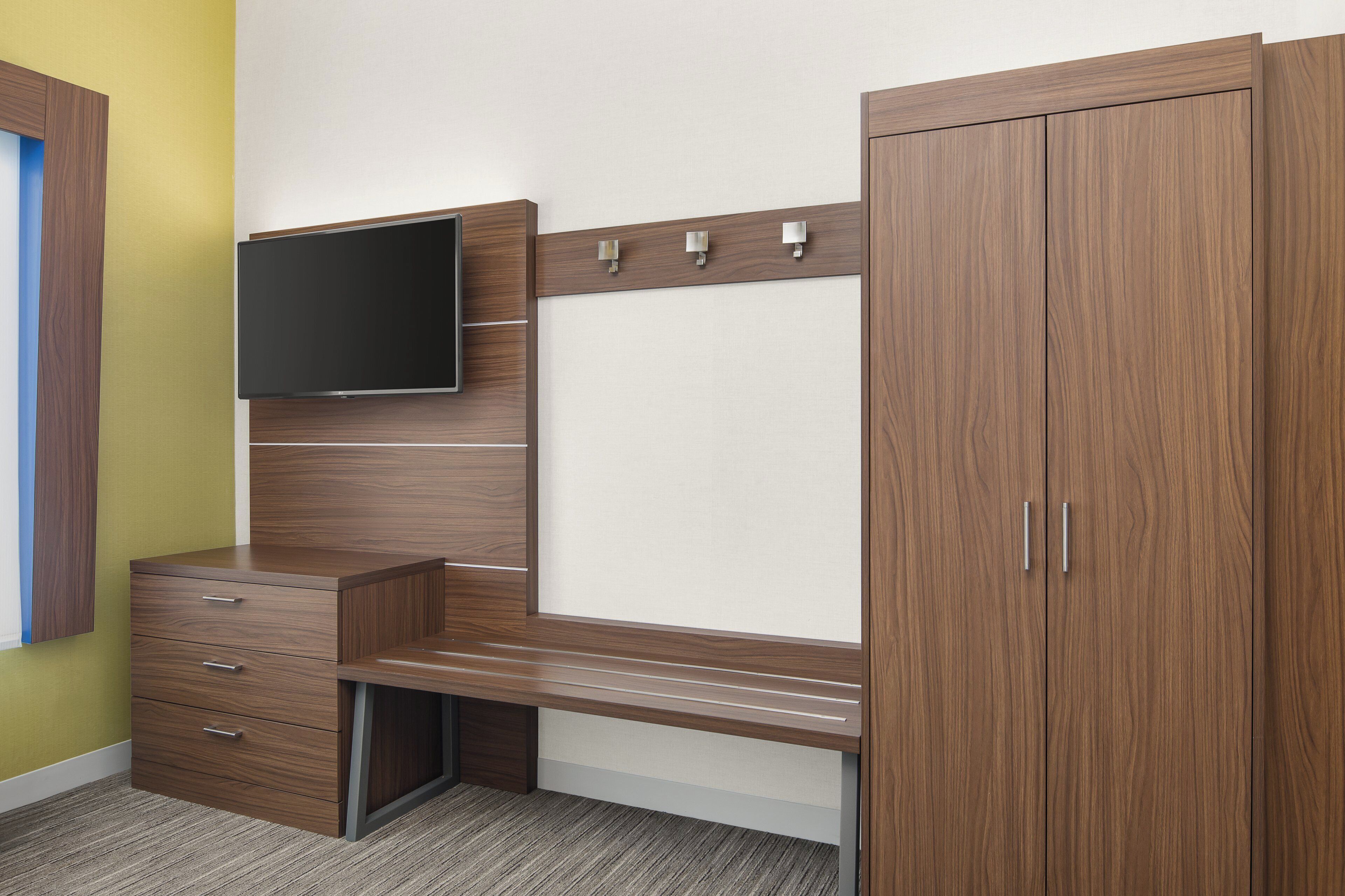A bedroom with a wooden desk, a television mounted on the wall, and a wardrobe.