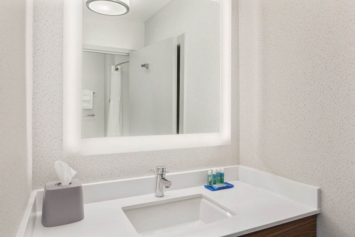 Un baño con lavamanos blanco, un espejo y un perchero para toallas.