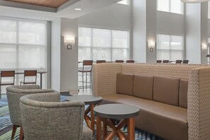 Een hotel lobby met een zithoek, tafels en grote ramen.