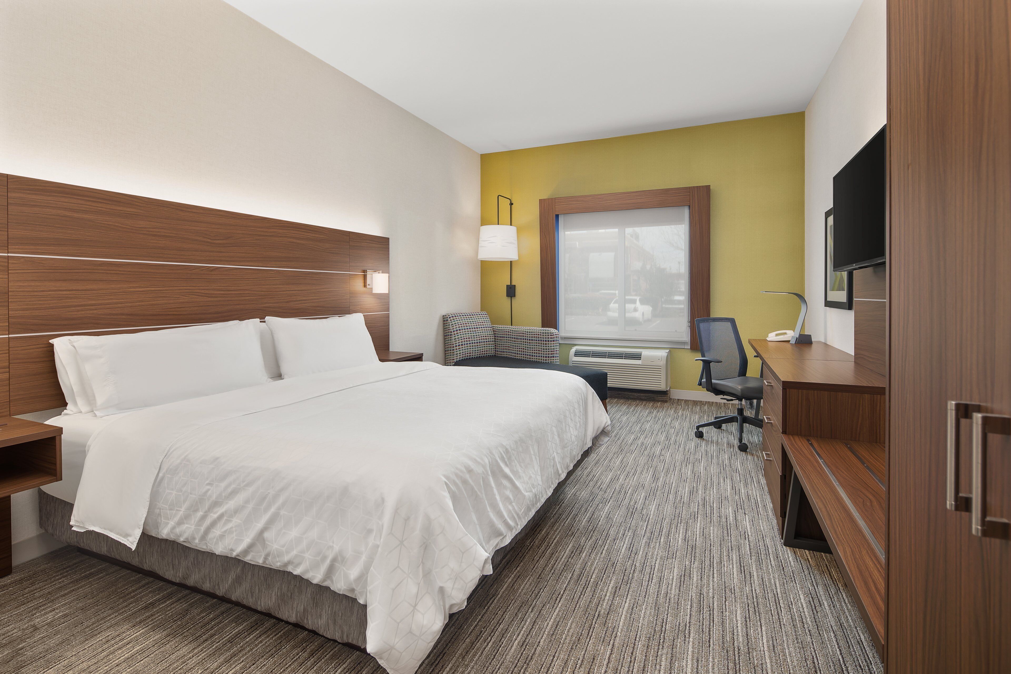 Une chambre d’hôtel avec un grand lit, un bureau, une chaise, une lampe et un téléviseur.
