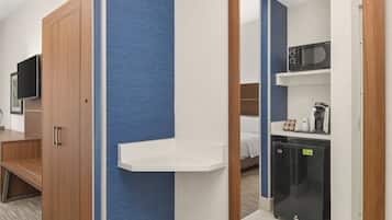 Habitación de hotel con armario de madera, televisor de pantalla plana, estante blanco, cama, refrigerador negro y microondas.