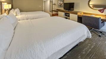 A hotel room with two beds, a desk with a chair, a television, and a mirror.