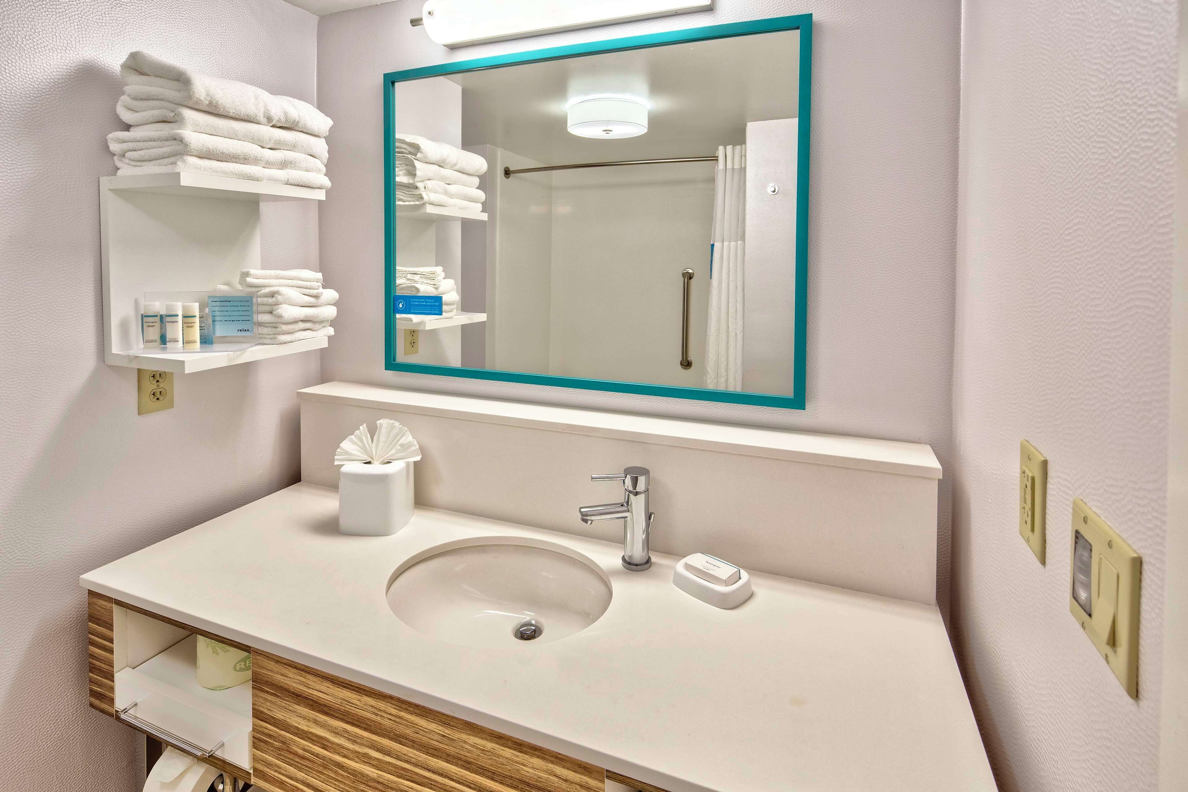 A bathroom with a sink, mirror, towel rack, and shelves with toiletries.