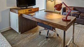 Una habitación de hotel moderna con un escritorio de madera, un televisor, una lámpara de escritorio roja y un sofá.