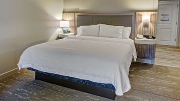 A hotel room with a large bed, two bedside tables, a nightstand, a wall-mounted lamp, and a door with a sign.