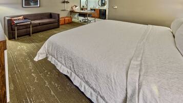 Ein Hotelzimmer mit einem großen Bett, einer Couch, einem Schreibtisch mit Stuhl und einer kleinen Küchenzeile.