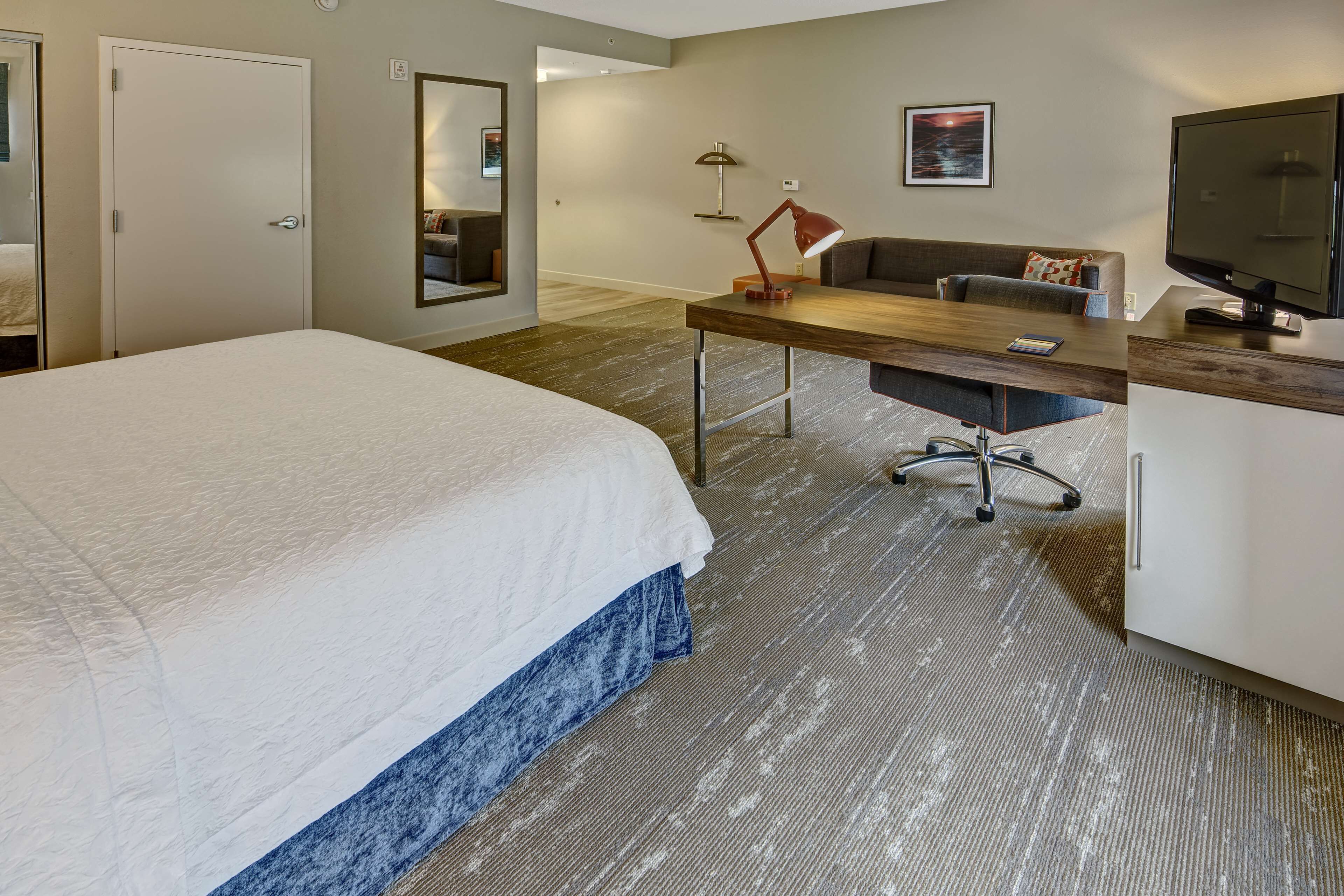 A hotel room with a large bed, a desk with a chair, a television, and a desk lamp.