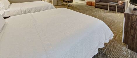 A hotel room with two large beds, a desk with a lamp, a sofa, a television, and a mirror on the wall.