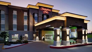 A Hampton Inn hotel entrance with a 'Welcome' sign, a covered driveway, and a landscaped area with small shrubs and a palm tree. - Hampton Inn Kingsville (Kingsville)