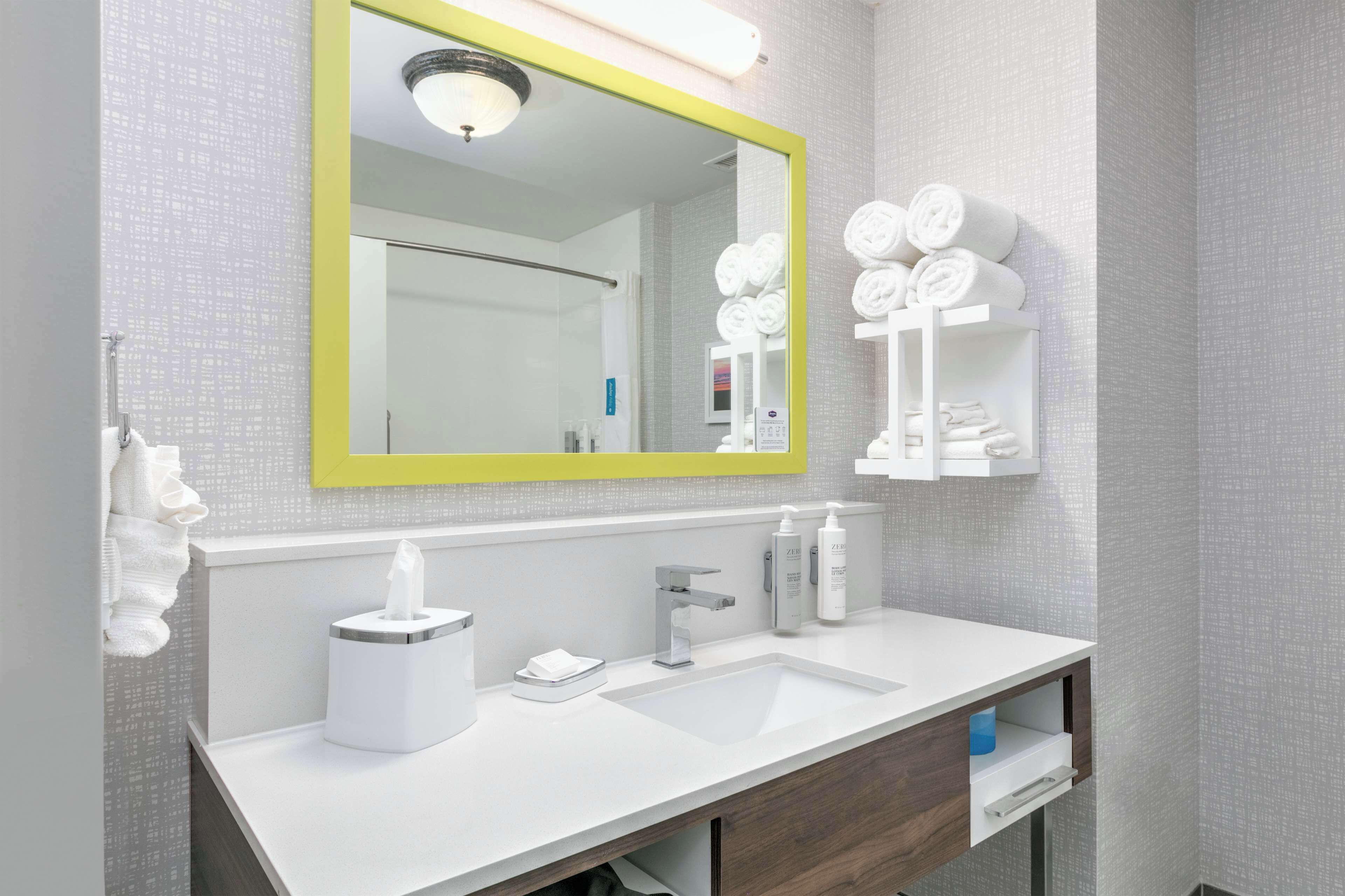 A modern bathroom with a white sink, a mirror with a yellow frame, and a towel rack with neatly folded towels.