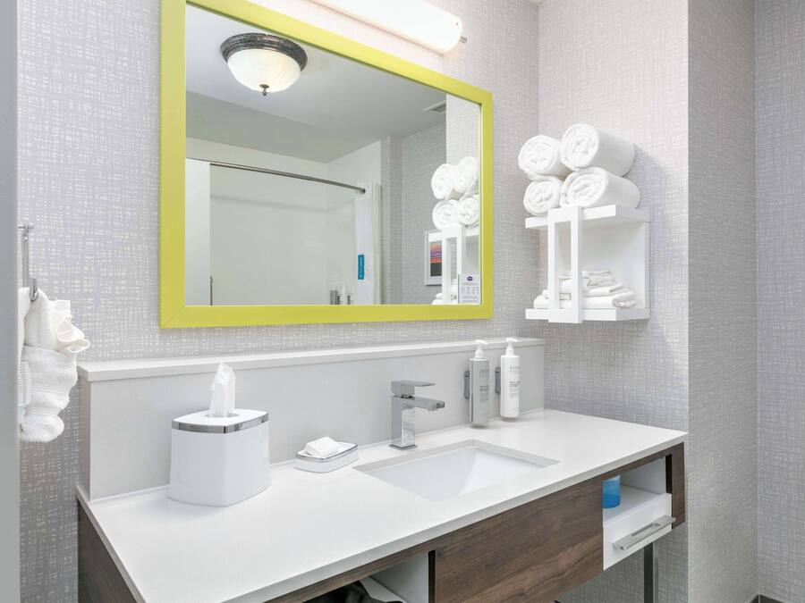 A modern bathroom with a white sink, a mirror with a yellow frame, and a towel rack with neatly folded towels.