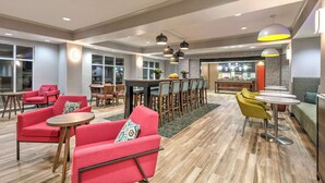 A modern hotel lobby with red and yellow seating, a central dining area, and a bar.
