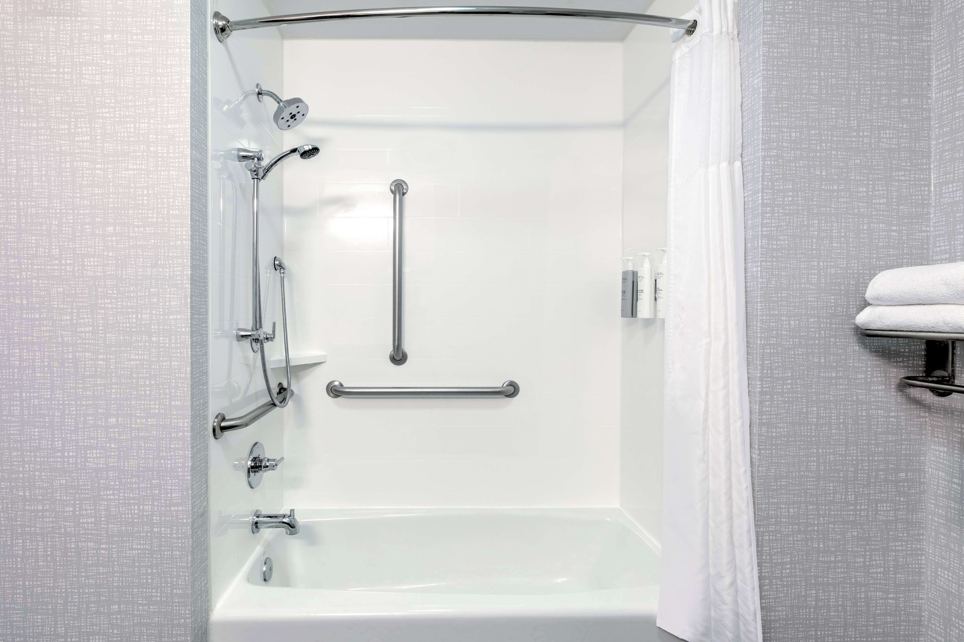 A modern shower area with a grab bar, a handheld showerhead, and a handheld showerhead.
