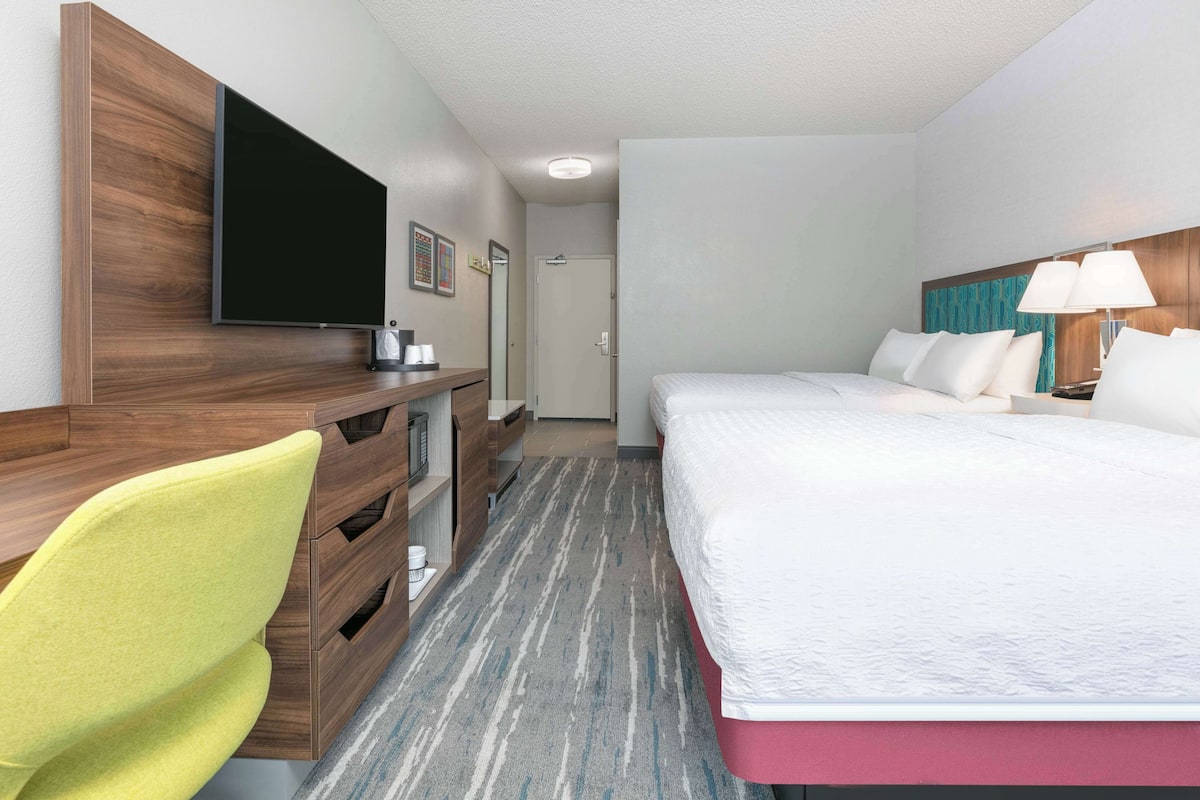 A hotel room with a bed, a desk with a flat-screen TV, a chair, and a nightstand.