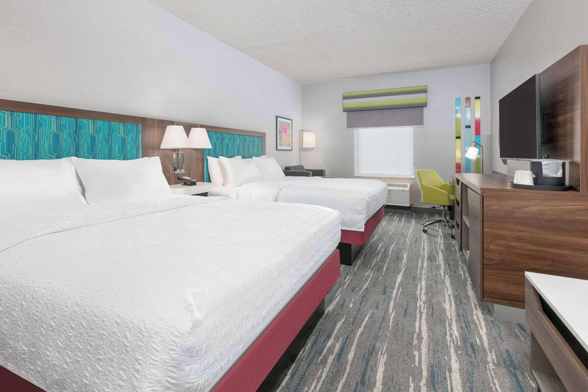 A hotel room with two beds, a desk, a chair, a TV, and a window with a view.