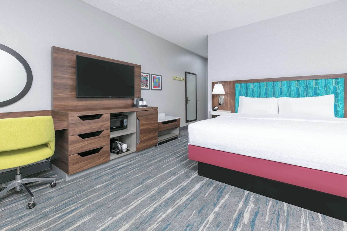 A hotel room with a bed, a desk with a chair, a television, and a bathroom.