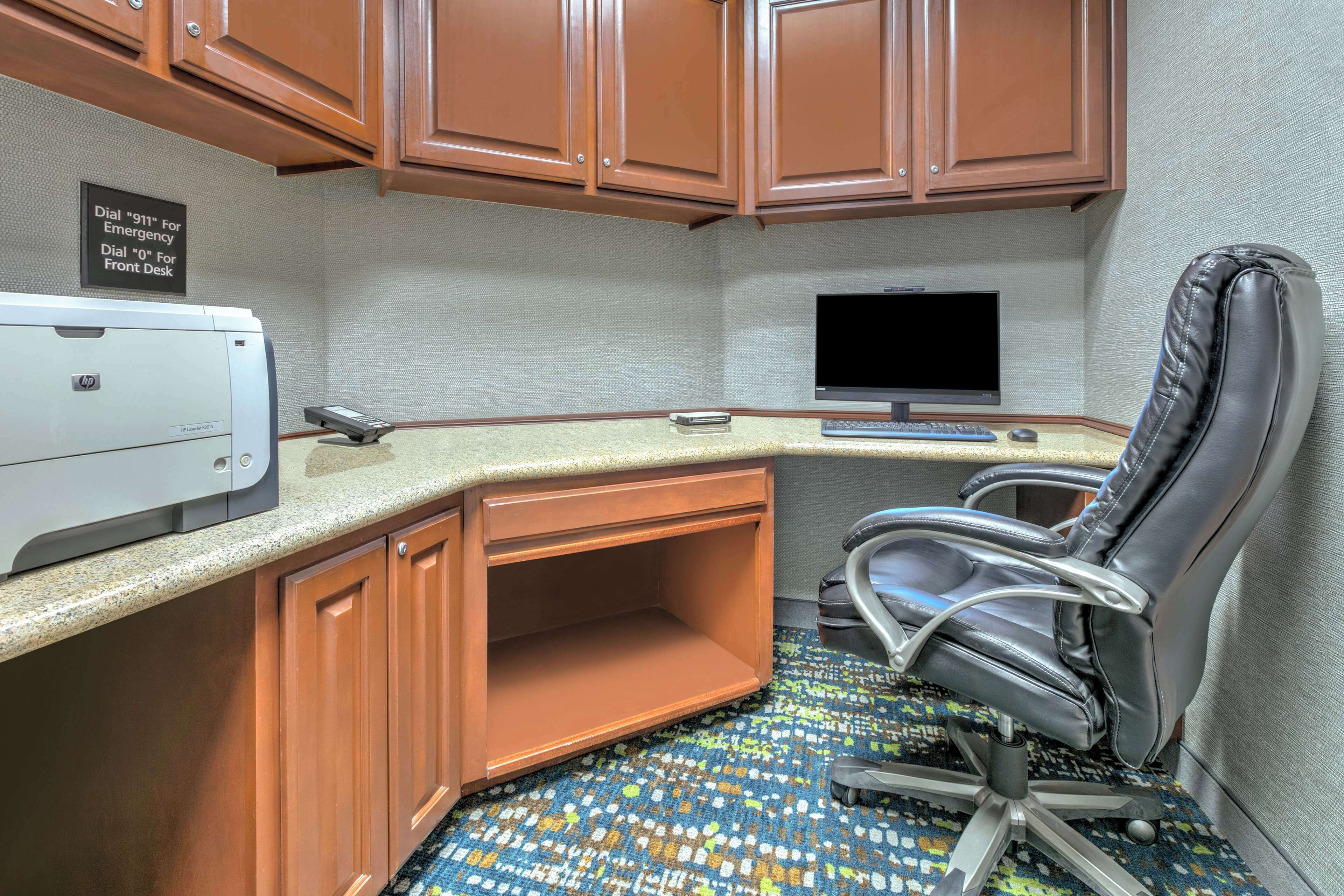 A compact office space with a desk, chair, printer, and a flat-screen monitor.
