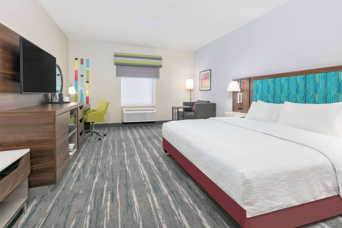 A hotel room with a bed, desk, chair, TV, and artwork on the walls.