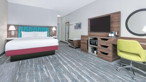 A hotel room with a bed, a desk, a chair, a TV, a mirror, and a microwave.