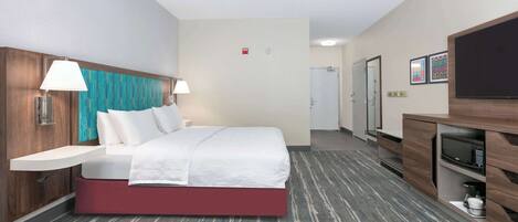 A hotel room with a bed, bedside tables, a TV, a microwave, and a small kitchenette.