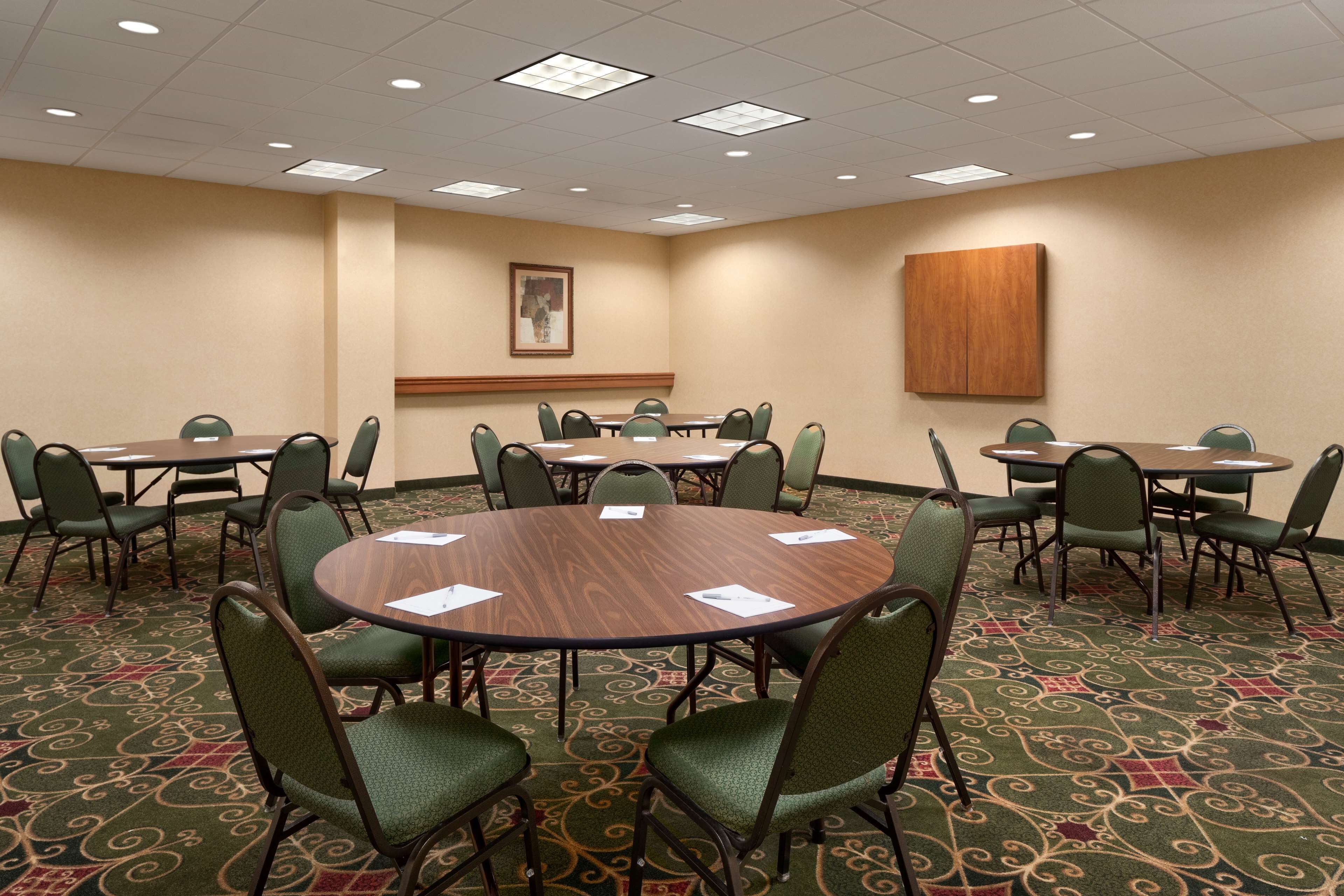 A conference room with multiple tables and chairs, carpeted floor, and ceiling lights.