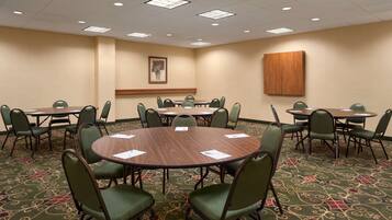 A conference room with multiple tables and chairs, carpeted floor, and ceiling lights.