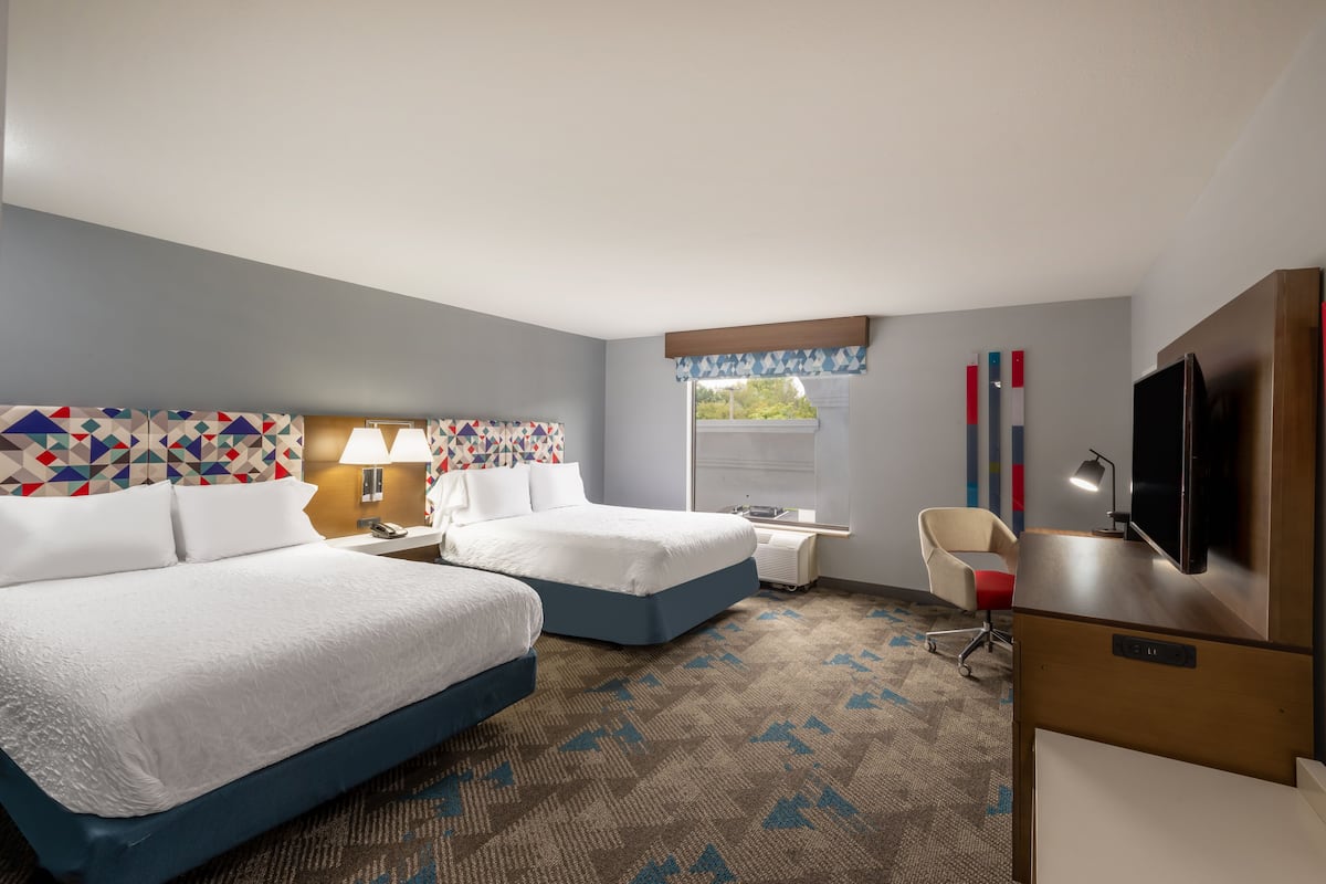 A hotel room with two beds, a desk, a chair, a television, and a window with a view.