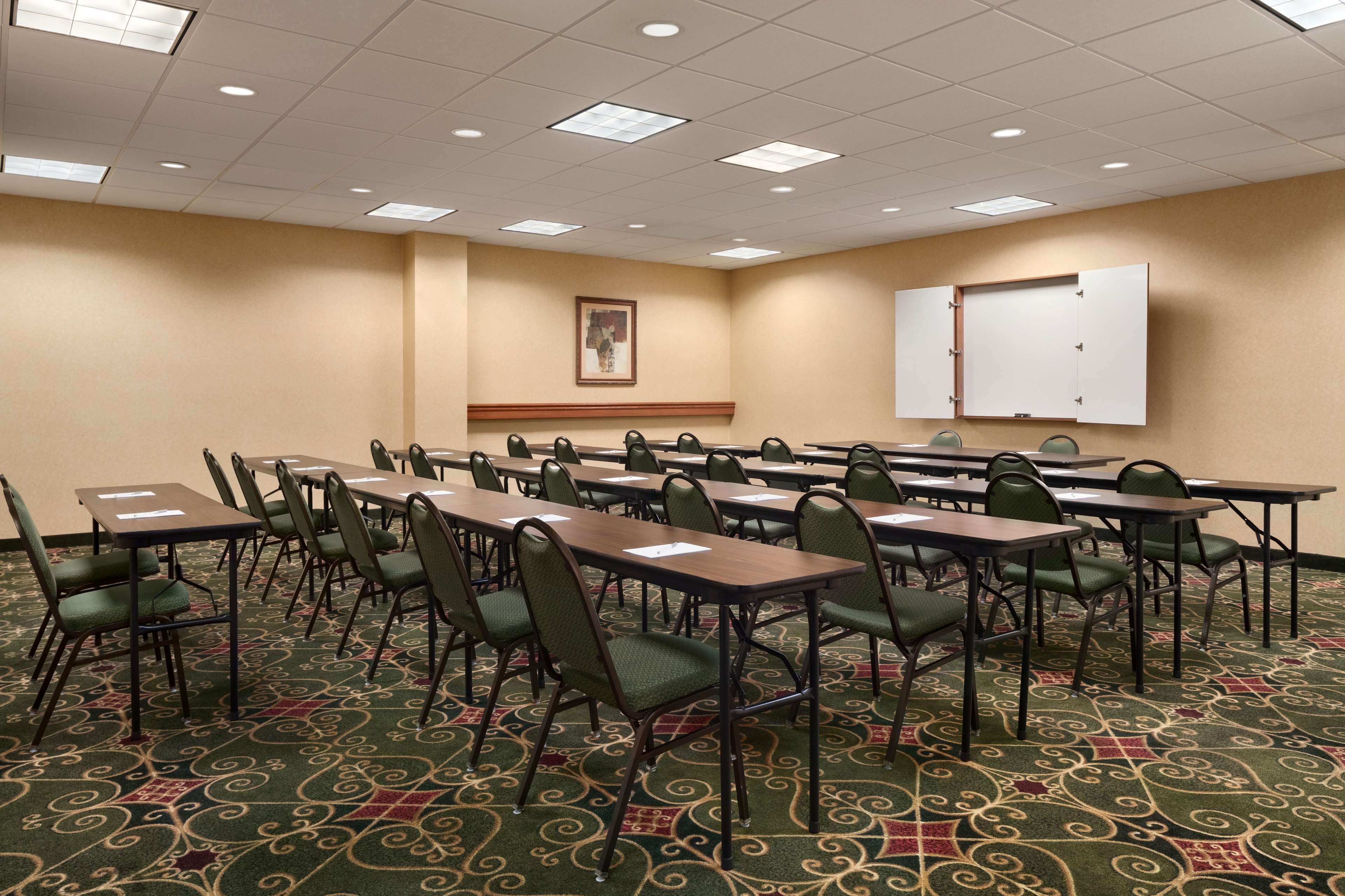 A conference room with multiple tables and chairs, a whiteboard, and a carpeted floor.