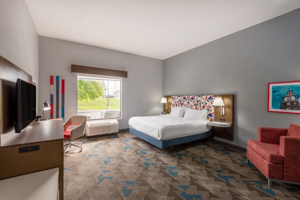 A hotel room with a bed, desk, chair, and a TV.