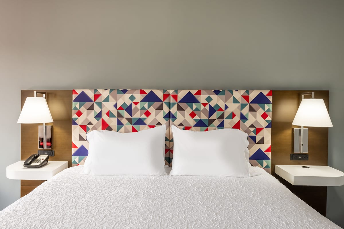 A hotel room with a bed, two bedside lamps, a phone, and a geometric-patterned headboard.