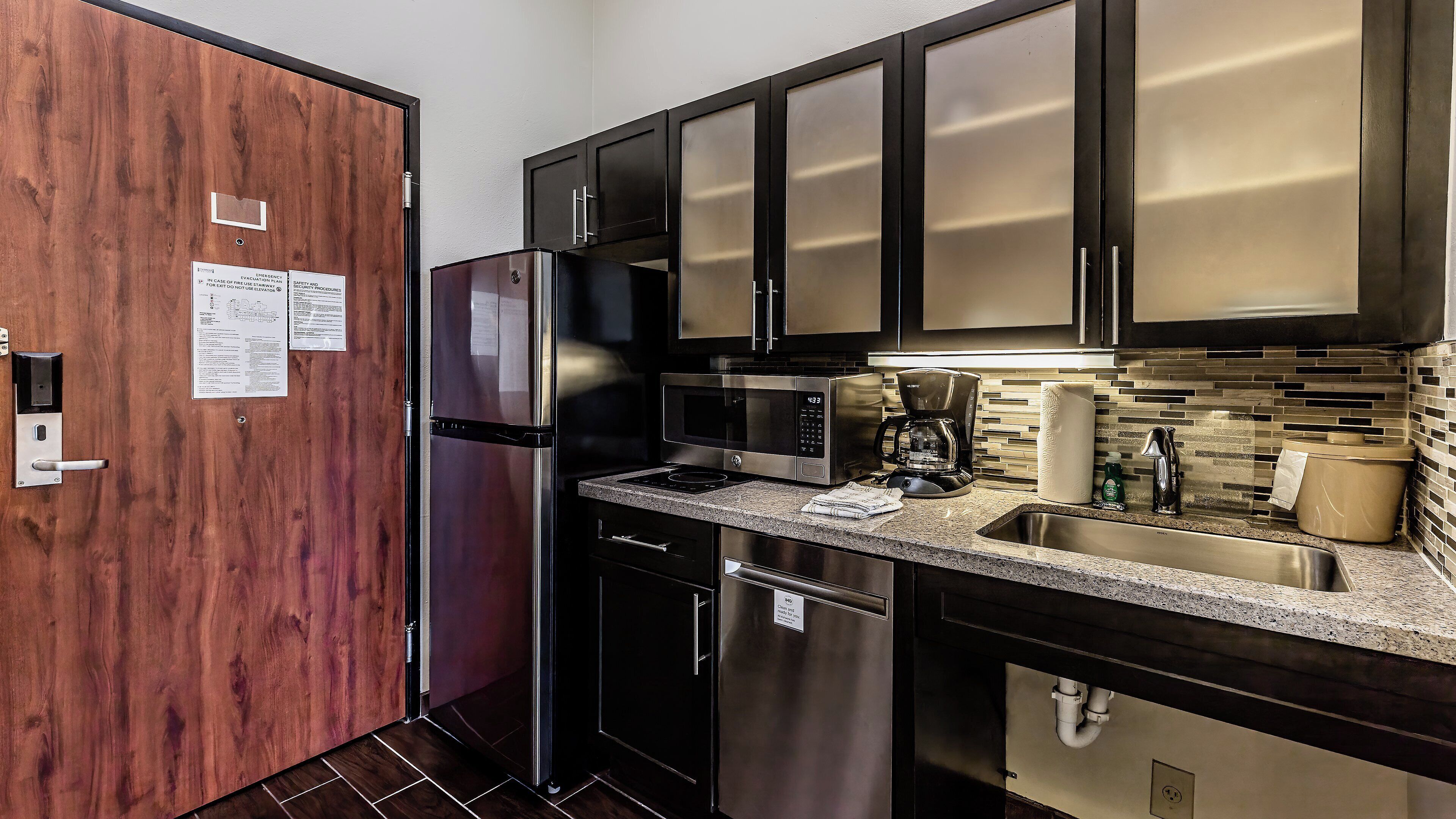 A modern kitchen with stainless steel appliances, a wood door, and a tiled backsplash.