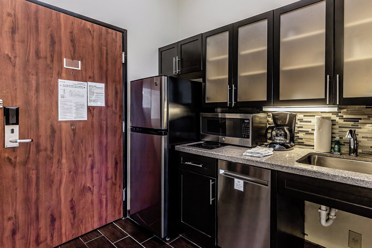 A modern kitchen with stainless steel appliances, a granite countertop, and a wood door.