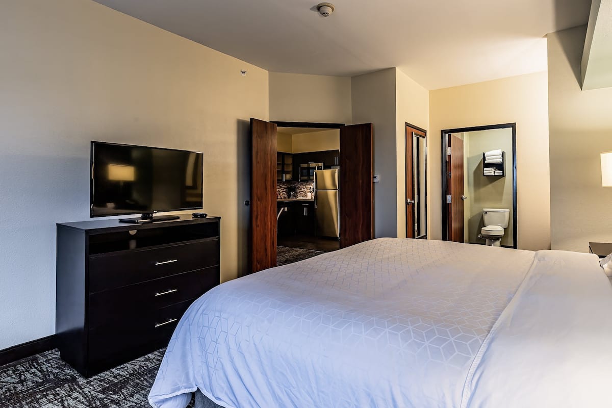 A hotel room with a bed, a TV, a dresser, a bathroom, and a kitchen area.