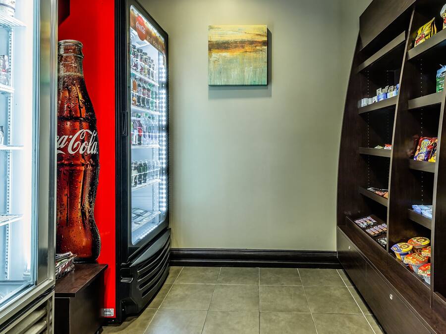 A narrow hallway with a Coca-Cola refrigerator on the left and shelves stocked with snacks on the right.