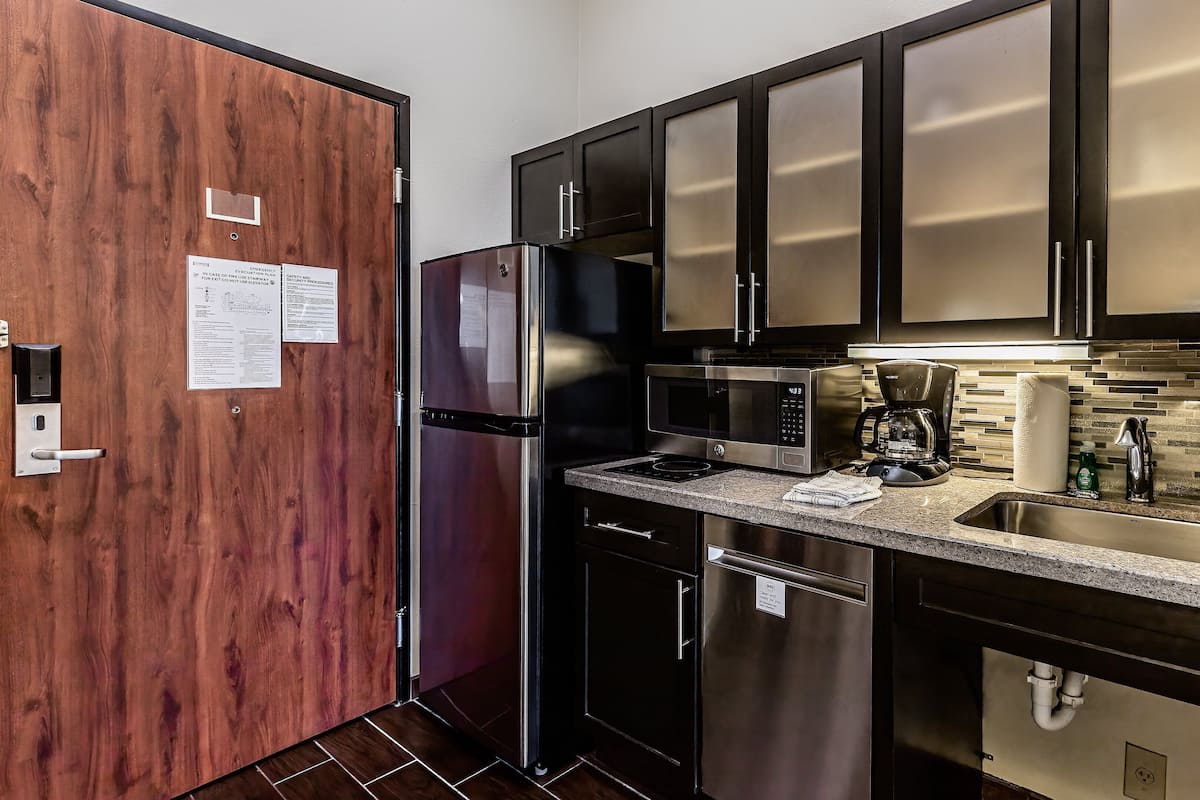 A modern kitchen with stainless steel appliances, a granite countertop, and a wood door.
