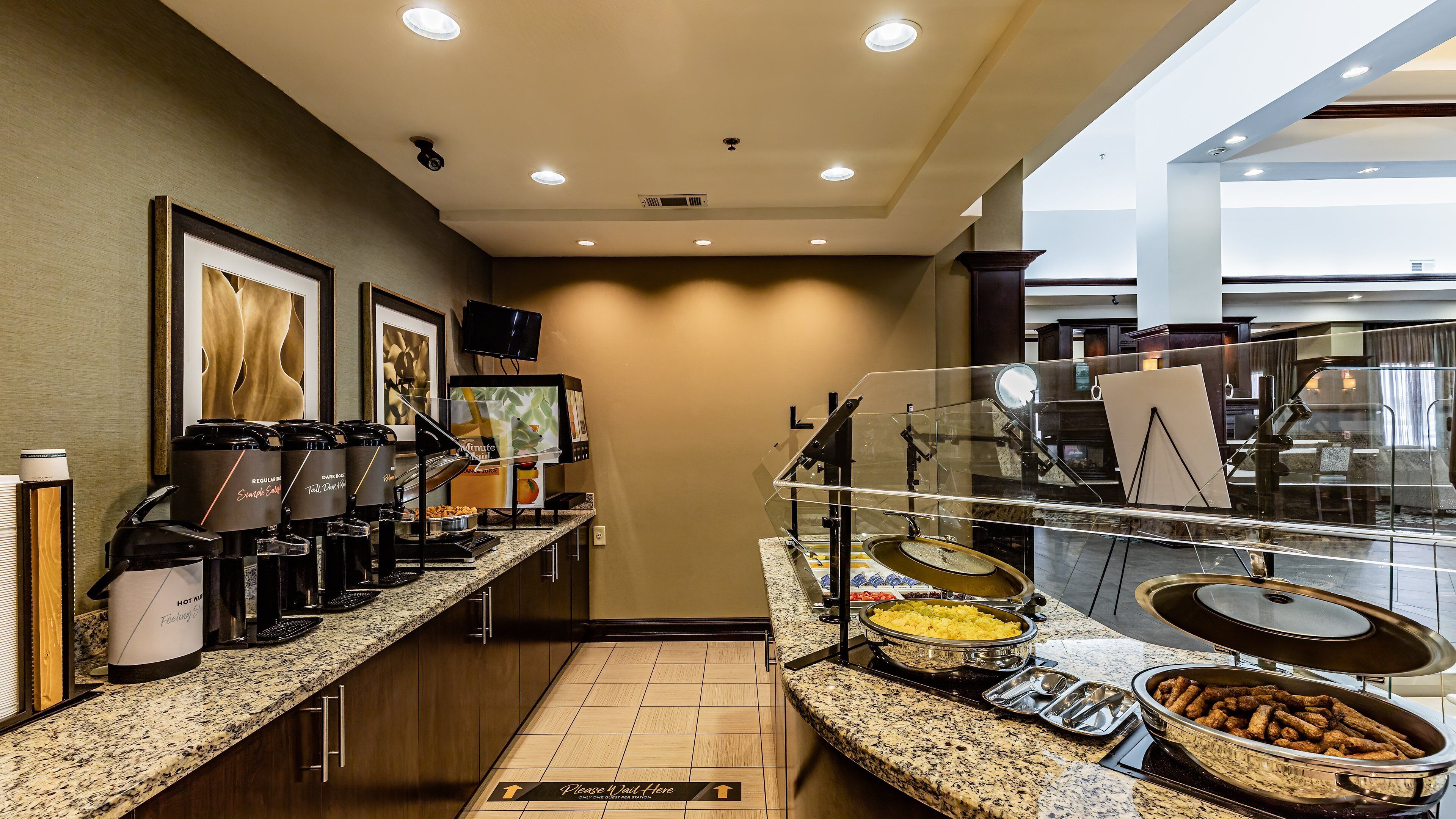 A breakfast buffet area with coffee makers, a TV, and various food items.