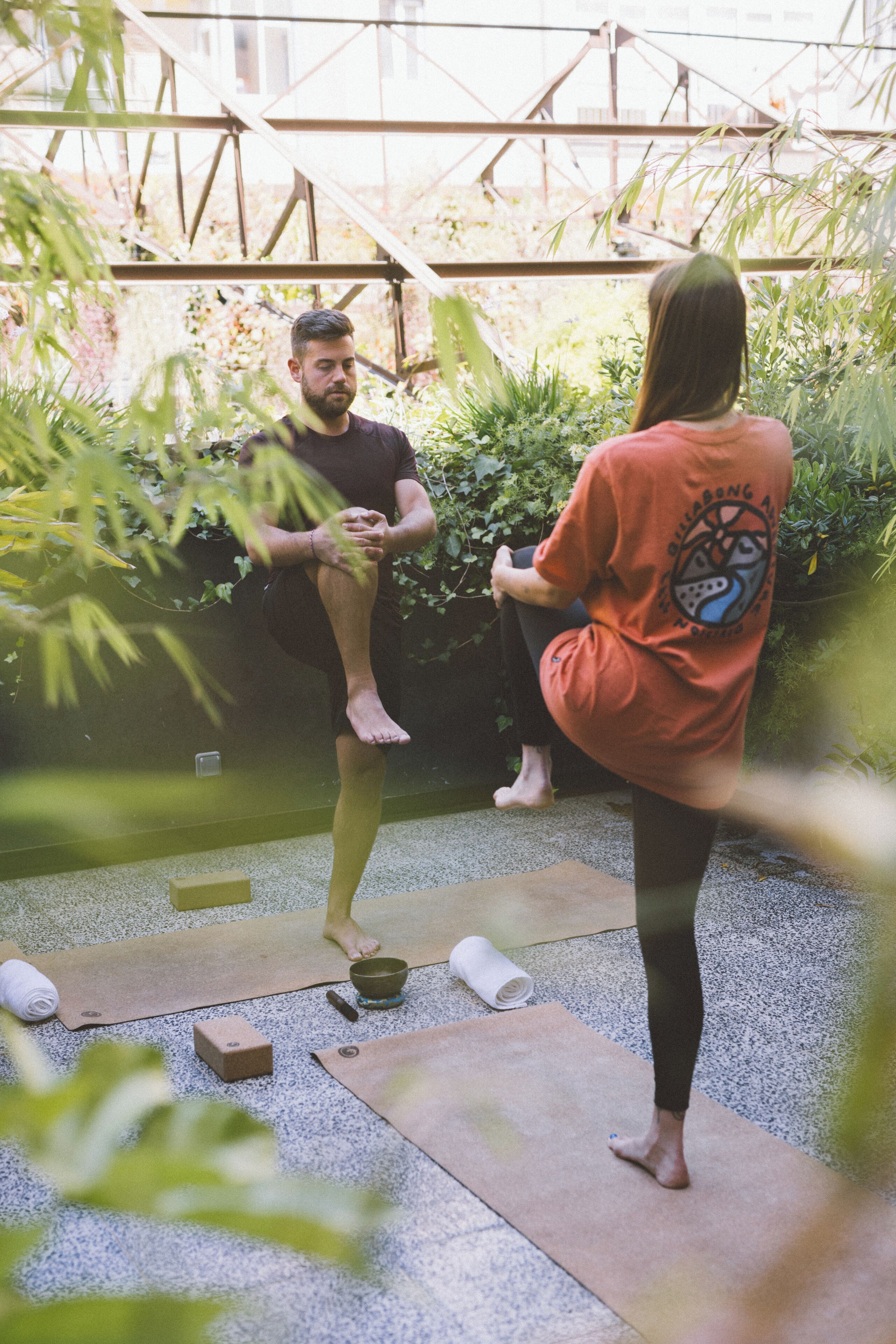 To personer dyrker yoga udendørs med yogamåtter og en skål på jorden.