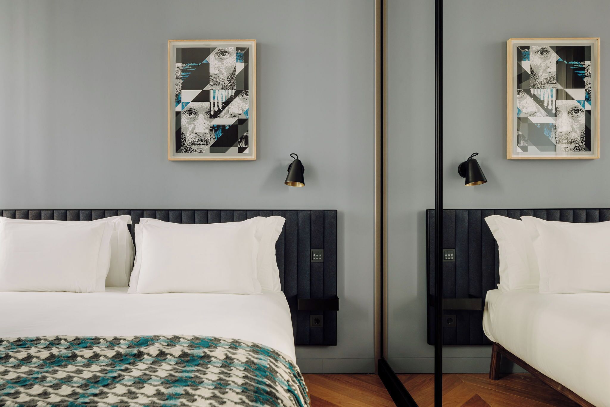 A hotel room with a bed, a mirror, and two framed artworks on the wall.