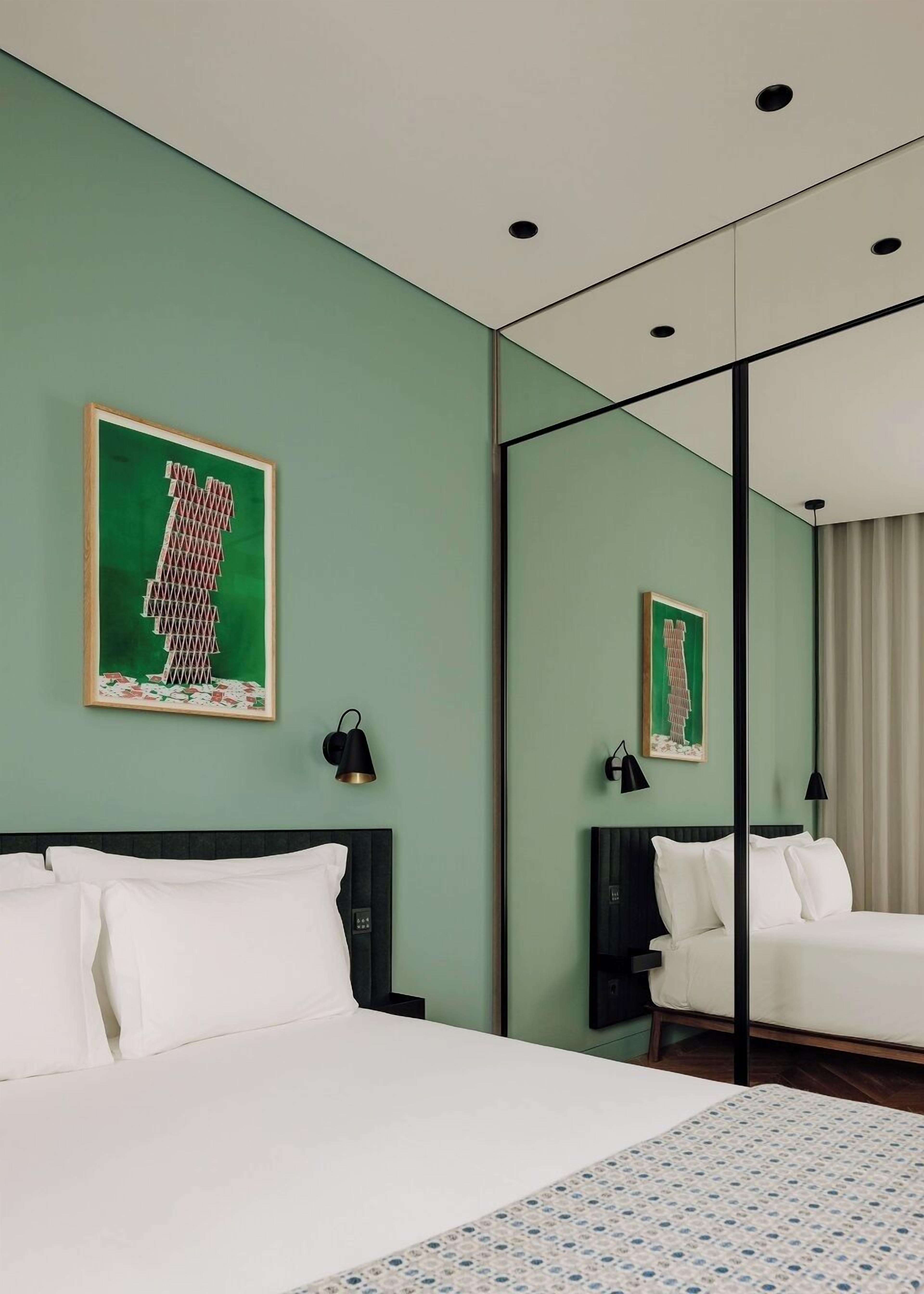 A hotel room with a large bed, a bedside table, a mirror, and artwork on the wall.