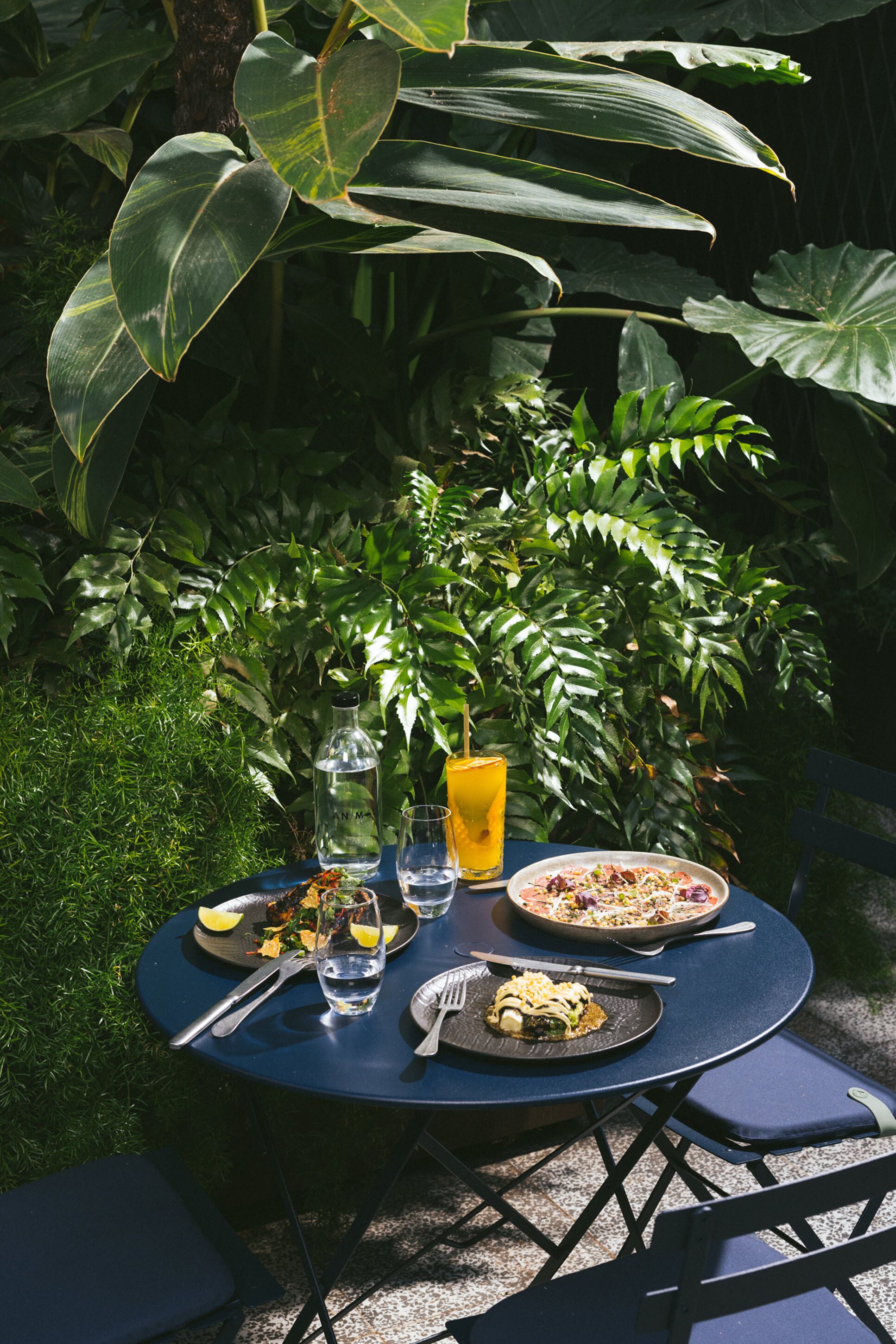 A round table set outdoors with a meal, a drink, and a bottle.