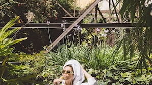 A person in a white robe sitting at an outdoor table with a drink and a plate of food, surrounded by greenery and a staircase. - Hotel X Hotel Avenida Liberdade, a Member of Design Hotels (Lisbon)