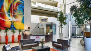 A modern lobby with a reception desk, leather sofas, a coffee table, and a colorful abstract painting. - Sunstays Lagoon Beach (Cape Town)