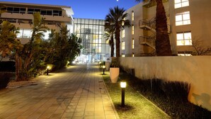A hotel entrance with a glass facade, palm trees, and a clear night sky. - Sunstays Lagoon Beach (Cape Town)